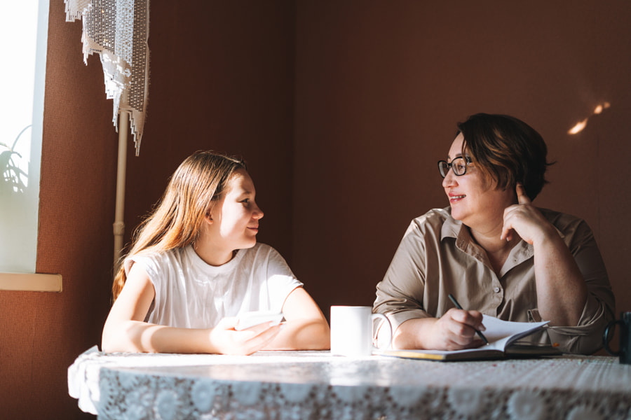 Working mother and teenager girl using mobile phone in kitchen at home by Galina Zhigalova on 500px.com