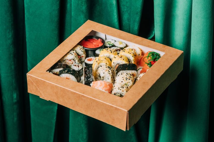 Box of sushi set against green curtains