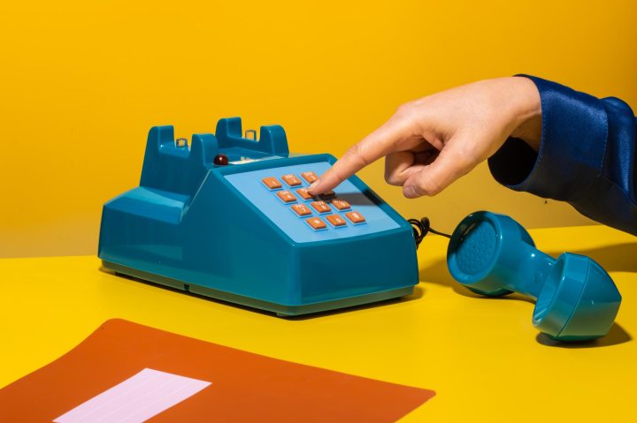 Unrecognizable person pushing buttons on retro stationary telephone near organizer against yellow background