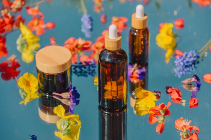 Cosmetic jar and bottles surrounded by flower petals on mirror with sky in reflection