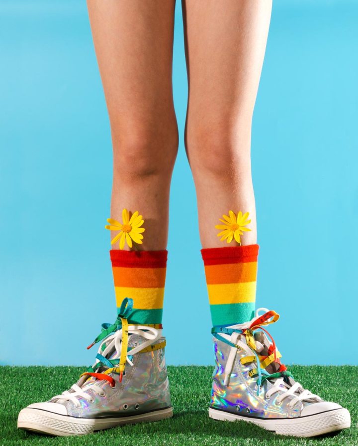 Cropped unrecognizable legs wearing vibrant striped socks and sneakers adorned with colorful ribbons