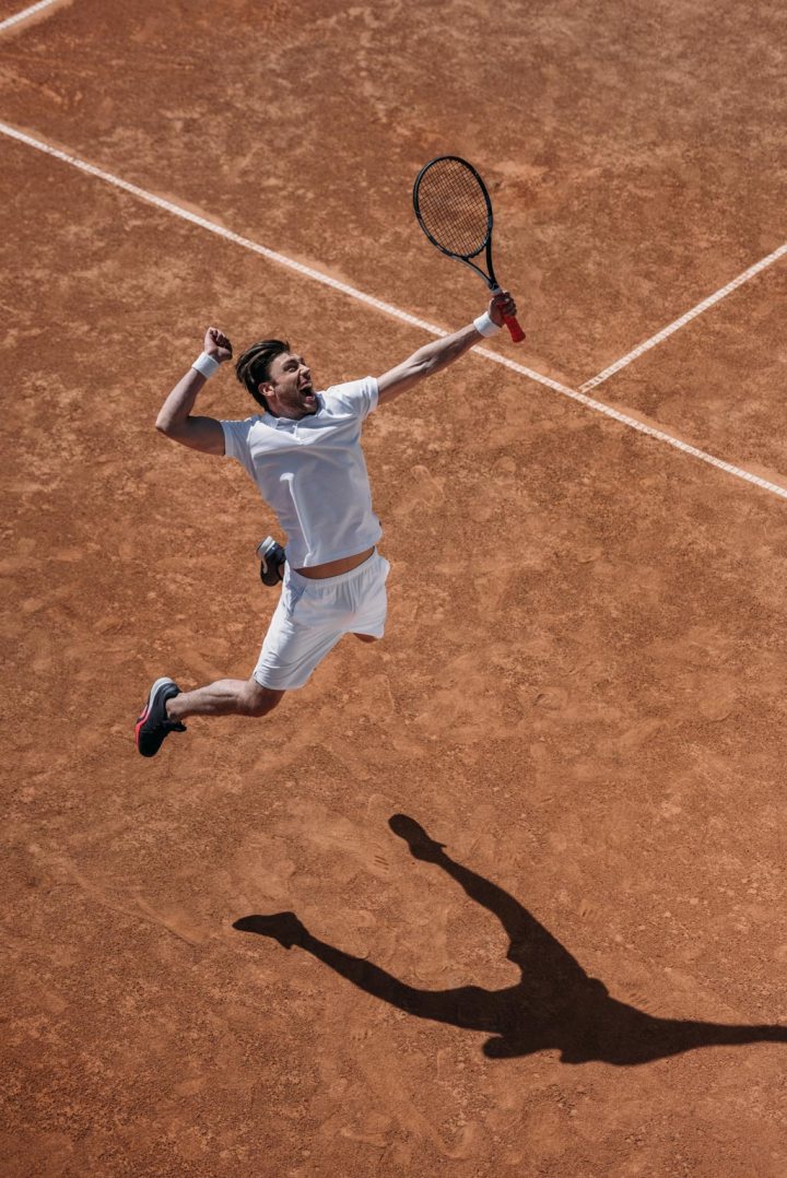 High angle view of athletic tennis player jumping in the air in celebration