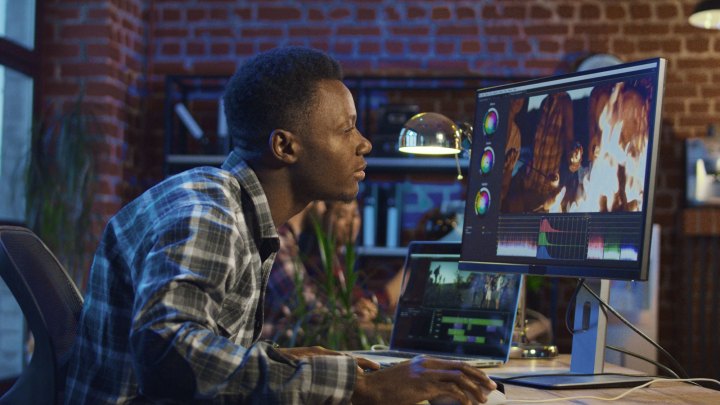 Side view of Black man working on computer and editing video with color correction