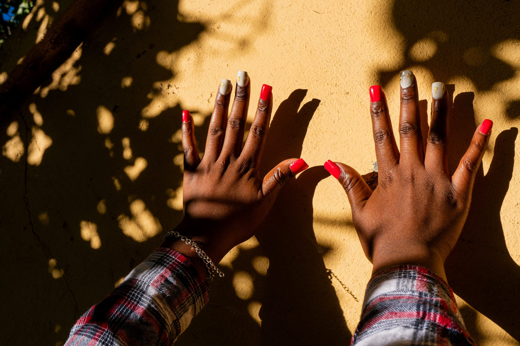 A close of up of a young African woman showing off nails against a yellow backdrop